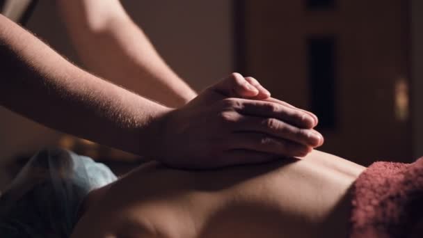 Un jeune masseur fait une cliente de massage professionnelle dans un salon de massage professionnel avec des bougies allumées dans une pièce sombre — Video