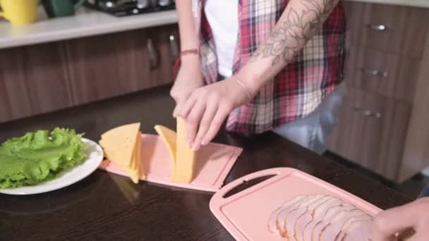 Närbild unga par man och kvinna gör smörgåsar i sitt kök. Begreppet hemlagad mat på egen hand. Långhårig modekille och tjej i köket — Stockvideo