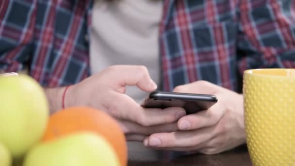 Una joven sonrisa pareja chico y una chica con el pelo largo sentarse en la mesa de la cena en la cocina y el uso de los teléfonos de comunicación con alguien en las salas de chat y redes sociales . — Vídeos de Stock