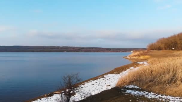 Luchtfoto van de oever van het meer deels in de sneeuw bij zonsondergang. Het concept van lokale reservoirs in het laagseizoen — Stockvideo