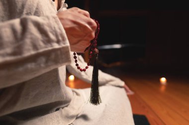 Antrenman ve meditasyon için giyinmiş yakın plan bir adam lotus pozisyonunda oturur ve loş ışıklı ahşap bir odada dikkat çekmek için kırmızı tespih tutar.