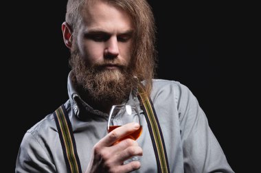 Uzun sakallı ve bıyıklı çekici bir adam duvarda oturmuş elini tutan bir bardaktaki alkollü içeceğin kokusunu kokluyor..