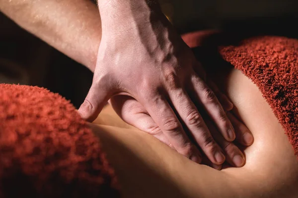 Close-up Cosmetología y fisioterapia. El masaje profesional a la parte inferior de la espalda de una mujer es hecho por un masajista. Concepto de terapia de manul y tratamientos de spa de masaje —  Fotos de Stock