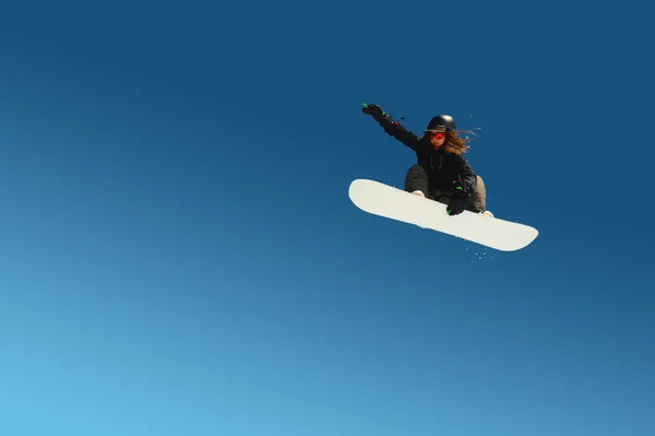 스노보더 걸은 파란 하늘을 잡고 점프하는 묘기를 부린다. 비행중에 외딴곳에 있는 푸른 색의 배경 운동 선수 — 스톡 사진