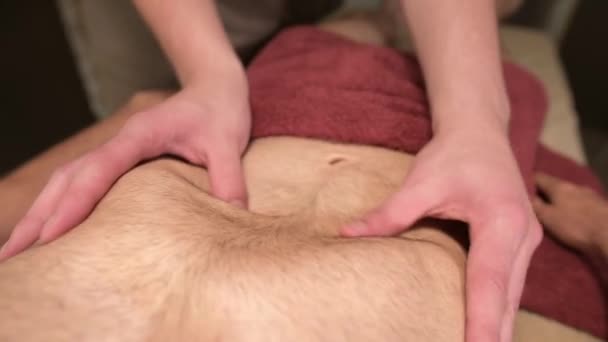 Männlicher Masseur massiert das Brustdiaphragma eines muskulösen männlichen Athleten in einem Massageraum mit dunkler Beleuchtung — Stockvideo