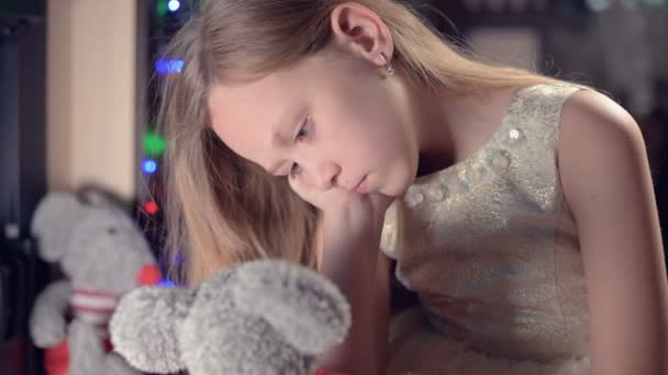 Una niña triste en un vestido rosa sola mira su juguete de peluche. Vacaciones malcriadas. Un niño melancólico — Vídeos de Stock