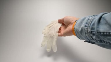 Kol saati ve kot pantolon giyen el, virüslerden ve salgınlardan korunmak için önlem ve güvenlik için eldiven giymenin gerekliliklerini açıklayan tıbbi beyaz eldivenleri gösteriyor.