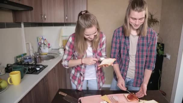 한 젊은 남녀가 부엌에서 샌드위치를 만듭니다. 집에서 요리하는 음식이라는 개념은 혼자서 만들어 집니다. 주방에서 장발의 패션을 하는 남자와 소녀 — 비디오