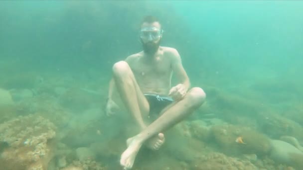 Slowly moving a young bearded man tries to meditate in a lotus pose at the bottom of the sea in the water. The concept of zen meditation and underwater yoga — Stock Video