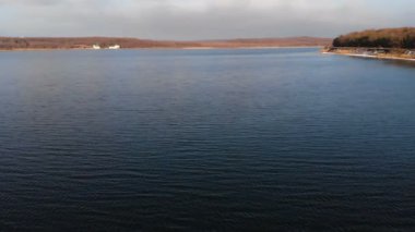 Gün batımından sonraki akşam alçaktan uçan bir dronun pürüzsüz yüzeyi üzerindeki hava görüntüsü. Yerel doğal su kaynağına sahip arka plan videosu