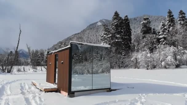 산 속의 겨울 숲 속에 벽이 거울로 가려져 있는 혁신적 인 하이테크 주택을 공중에서 본 것이다. 산에서의 생태 관광의 개념. 자연 보호구역의 현대 건축 양식 — 비디오