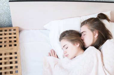 Bir çift modern erkek ve kadın beyaz yataklarında sarılarak uyuyorlar. Genç ve modern aile kavramı ve uyku sorunları