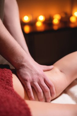 Kaplıca salonunun karanlık odasındaki kadın kalçasına mum yakmanın arka planına karşı yakın plan profesyonel masaj. Kalça kası sağlığı kavramı