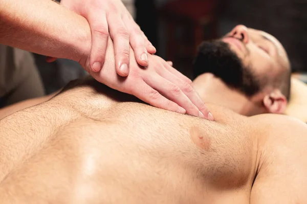 Een close-up mannelijke masseur doet een sportieve massage van de borstspier aan de cliëntsporter in een professionele massagesalon. Het concept van borstspier en borstspier gezondheid — Stockfoto