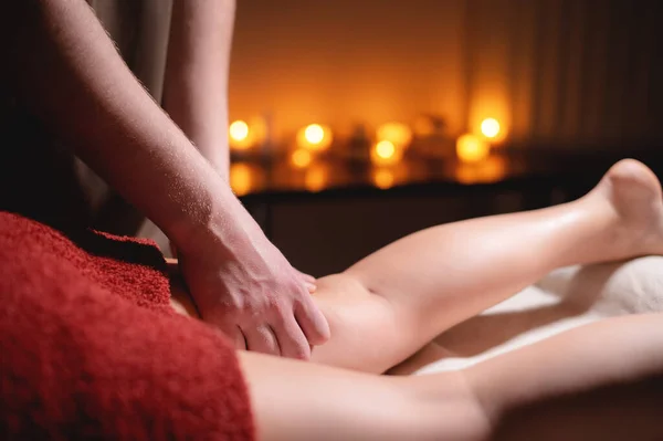 Närbild professionell massage av den kvinnliga höften i det mörka rummet i spa salongen mot bakgrund av brinnande ljus. Begreppet höftmuskel hälsa — Stockfoto