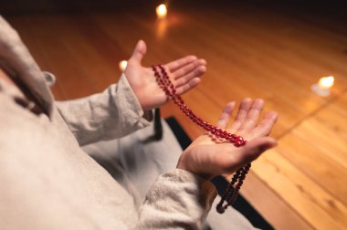 Rahiplerin elleri, çalışma odasının ahşap zeminine karşı kırmızı tespihleri tutar ve mum yakar.