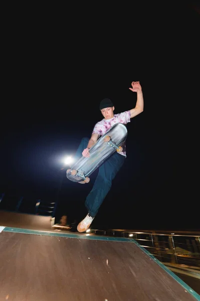 Молодой фигурист делает трюк, скользя ночью в скейтпарке. Концепция ночного отдыха и молодежной культуры в ночное время — стоковое фото