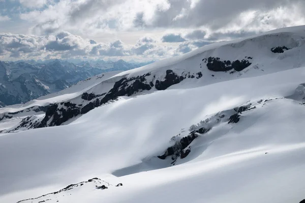 Montanhas altas cobertas de neve com geleira e rochas contra o céu noturno e cordilheira com nuvens à distância — Fotografia de Stock