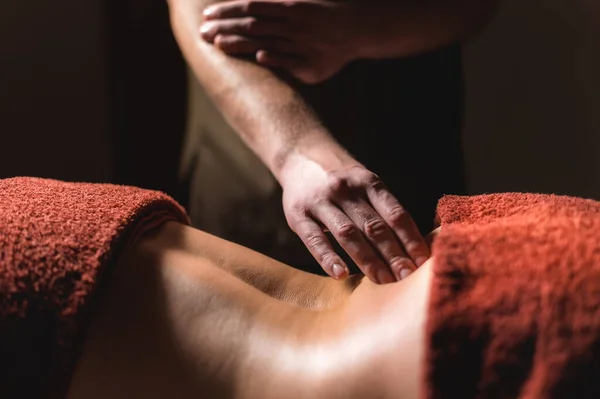 Professional massage of the back and lower back. Male masseur massages a client to a woman in a dark room by candlelight