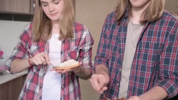 Ett ungt par gör smörgåsar i köket. Begreppet hemlagad mat på egen hand. Långhårig modekille och tjej i köket — Stockvideo