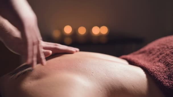 Massage professionnel du dos et du bas du dos. Masseur masculin masse un client à une femme dans une pièce sombre aux chandelles — Video