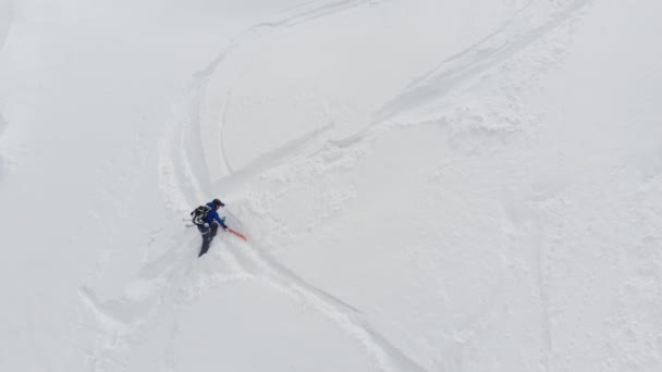 Вид с воздуха на спортсмена-мужчину, карабкающегося вверх по крутому склону. Skitour фрирайд Backcountry восхождение на лыжах через снег высоко в горах Северного Кавказа — стоковое видео