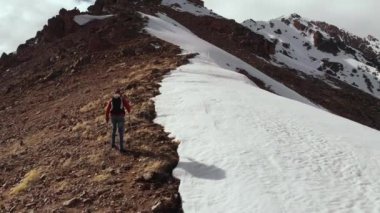 Tırmanışçı bir sırt çantasıyla tepeye tırmanır ve kayayla karın birleştiği tepede yürüyüş çubukları vardır. Kuzey Kafkasya 'nın yüksek dağlarında hava manzarası