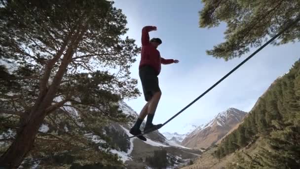 Un giovane uomo striscia su una slackline tra le montagne del Caucaso settentrionale. Slackline en sfondo delle montagne — Video Stock