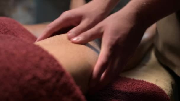 Close-up Massagem esportiva profissional no quadril. Um massagista do sexo masculino massageia um atleta masculino em uma sala com luz ofuscada contra o fundo de velas acesas. — Vídeo de Stock