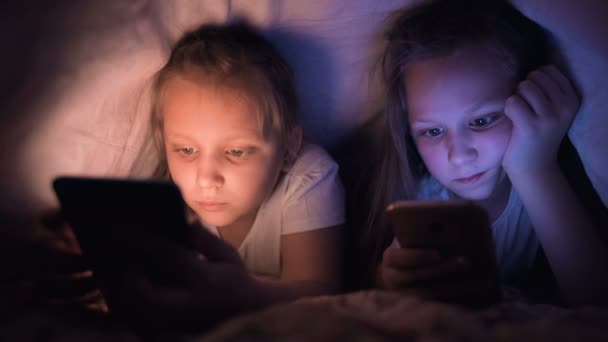 Şaplak atan iki küçük kız battaniyenin altında uyumaz. Çocuklar için uykusuzluk ve internet bağımlılığı cihazlar ve cihazlar — Stok video