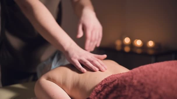 Un jeune masseur fait une cliente de massage professionnelle dans un salon de massage professionnel avec des bougies allumées dans une pièce sombre — Video