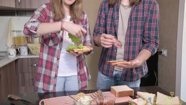 A young couple man and woman make sandwiches in their kitchen. The concept of home-cooked meals on your own. Long-haired fashion guy and girl in the kitchen