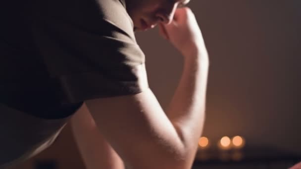 Ein junger männlicher Masseur führt in einem professionellen Massagesalon mit brennenden Kerzen in einem dunklen Raum eine professionelle Ellbogenmassage für ein Kundenmädchen durch — Stockvideo