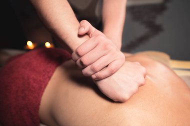 Genç bir masör, kaslı bir atlete spor masajı yapıyor. Mumlarla dolu karanlık bir odada profesyonel sırt masajı. Kas aparatının gevşemesi ve kaplıcada iyileşmesi