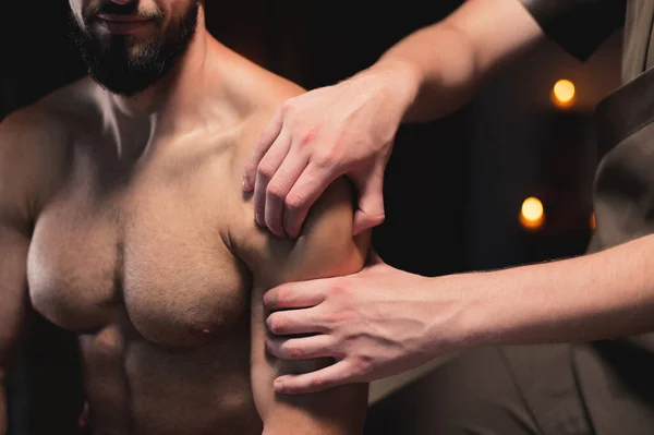 Zbliżenie mężczyzna masażysta robi sportowe masaż ramion do umięśniony mężczyzna sportowiec w pokoju z kontrastującym ciemnym świetle. Profesjonalny masaż sportowy — Zdjęcie stockowe