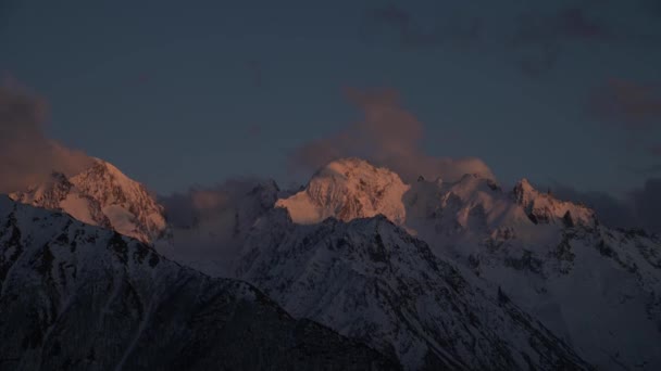 Timelapses van hoge besneeuwde bergen en wolken hoog in de bergen van de noordelijke Kaukasus na zonsondergang. De laatste zonnestralen op de bergen van het begin van de nacht — Stockvideo