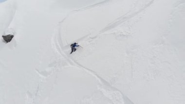 Dik bir yamaca tırmanan erkek bir kayakçının hava manzarası. Kuzey Kafkasya 'nın yüksek dağlarında kayaklarla kayak yaparak Skitour beleşçilik yapıyor.