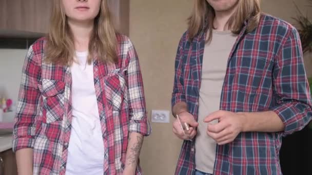 Una giovane coppia uomo e donna fanno panini nella loro cucina. Il concetto di pasti fatti in casa da soli. Ragazzo di moda dai capelli lunghi e ragazza in cucina — Video Stock