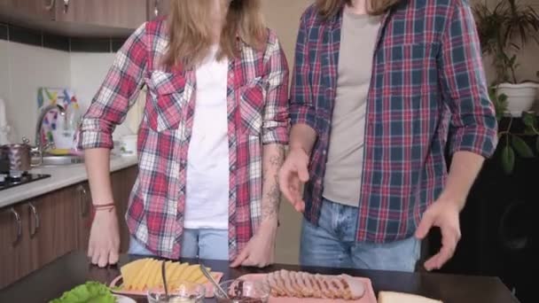 Una joven pareja de hombres y mujeres hacen sándwiches en su cocina. El concepto de comidas caseras por su cuenta. Cortar la carne y las verduras juntas para hacer sándwiches — Vídeos de Stock