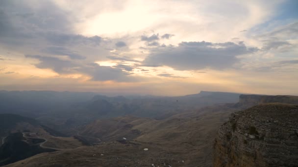 O pôr-do-sol cai de um penhasco alto ao lado de um penhasco. Vista do vale com serpentinas estradas de montanha e montanhas — Vídeo de Stock