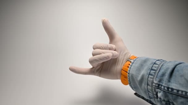 Mão na luva médica branca no fundo branco mostra gesto dedo mostra o gesto shaka. O gesto dos surfistas e amantes da liberdade e da vida extrema — Vídeo de Stock