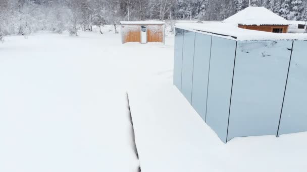 Aerial view of an innovative hi-tech house with mirrored transparent walls in winter near a coniferous forest in the mountains of the Caucasus or the Alps. — Stock Video