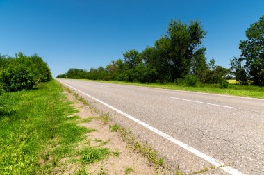 Yazın asfalt yolda yol kenarlarında mavi gökyüzüne karşı yeşil çimenler ve ağaçlar vardı. Ulaşım ve ulaşım lojistik şirketleri için güneşli bir gün.