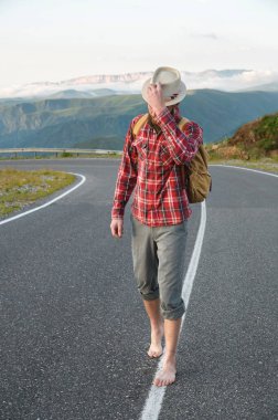 Tişört şapkalı ve çıplak ayaklı genç sakallı bir hippi dağlarda bir köy yolunda yürüyor. Otostop ve bedava seyahat