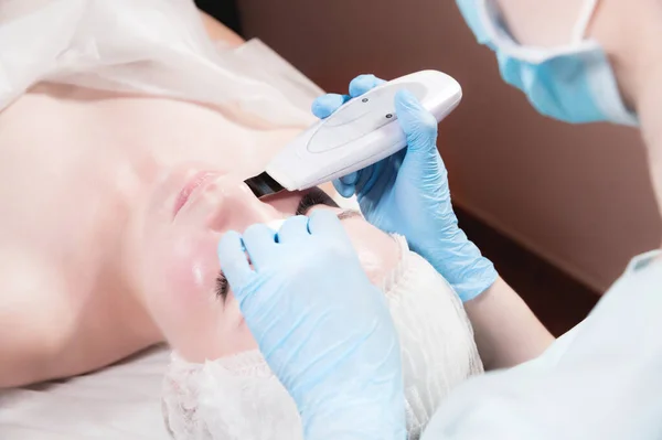 A professional beautician makes an ultrasonic face cleaning to a client in a beauty salon — Stock Photo, Image