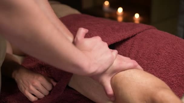 Zbliżenie Profesjonalny sportowy masaż bioder. Męski masażysta masuje męskiego sportowca w pokoju z przyćmionym światłem na tle płonących świec. — Wideo stockowe