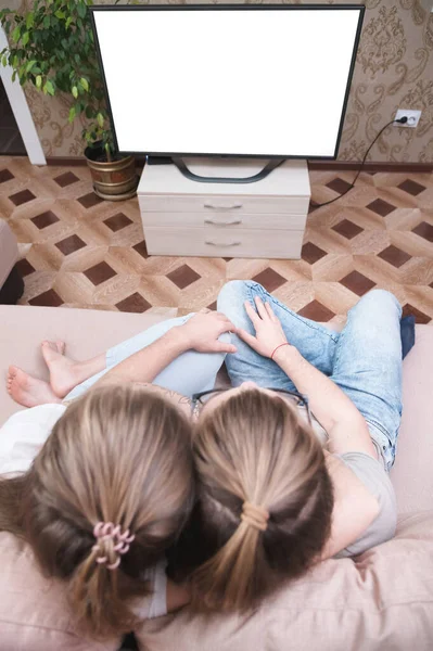 Приваблива молода довгошерста пара обіймає диван вдома в ізоляції, дивлячись телевізор. Концепція проведення часу з близькими під час пандемії . — стокове фото