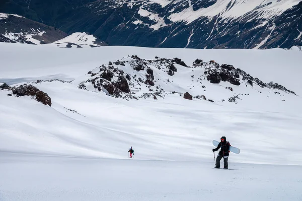 Two woman snowboarder climbs the mountain through the snow backcountry with a snowboard behind her shoulders. Climb the mountain for freeride — Stock Photo, Image