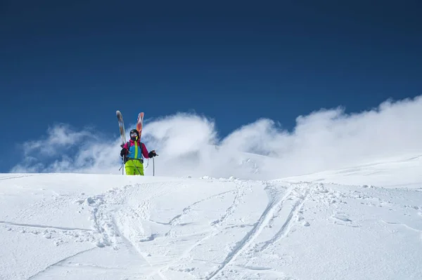 Portret van een vrouwelijke skiër in een veelkleurig, helder jasje met een skimasker met haar gezicht dicht op een zonnige dag tegen de achtergrond van besneeuwde Kaukasische bergen en wolken — Stockfoto