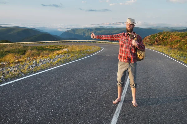 Tişört şapkalı ve çıplak ayaklı genç sakallı bir hippi dağlarda bir köy yolunda yürüyor. Otostop ve bedava seyahat